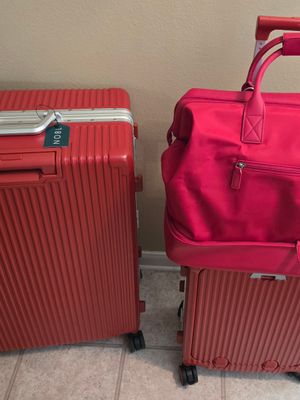 Customer-uploaded image. Click to see more details. The image represents: Three red luggage pieces arranged together: two large hard-shell suitcases with ribbed texture and wheels, and one bright pink soft-sided duffel bag with handles positioned on top of the smaller suitcase.